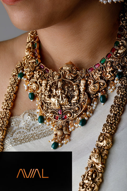 indian bride wearing full temple jewelry set including choker, long haar, earrings, and maang tikka in antique gold